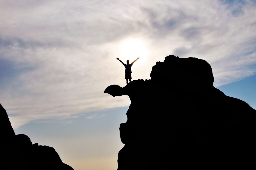 Silhouette of a person standing triumphantly on a rock peak against the sky, representing career success