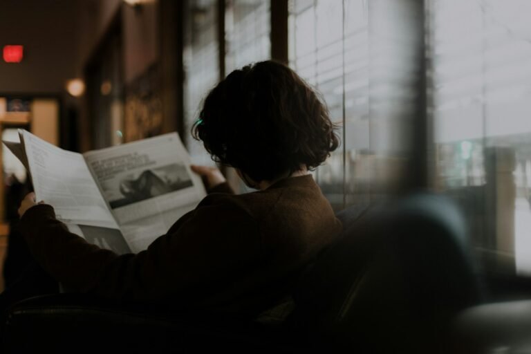 Woman sitting by a window reading printed pages, as when learning how to read a Vedic astrology report